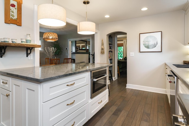 678 S Cassingham Rd, Columbus, OH 43209 - kitchen with arched walkways, dark wood-style floors, white cabinets, appliances with stainless steel finishes, and dark stone counters