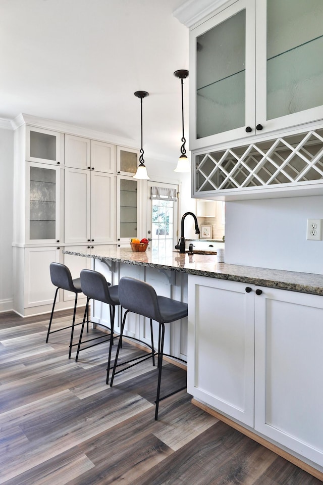 274 E Jenkins Ave, Columbus, OH 43207 - kitchen featuring stone countertops, a breakfast bar, hanging light fixtures, dark wood finished floors, and glass insert cabinets