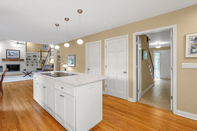 7661 Norhill Rd, Columbus, OH 43235 - kitchen with black electric cooktop, a brick fireplace, light wood finished floors, and a center island