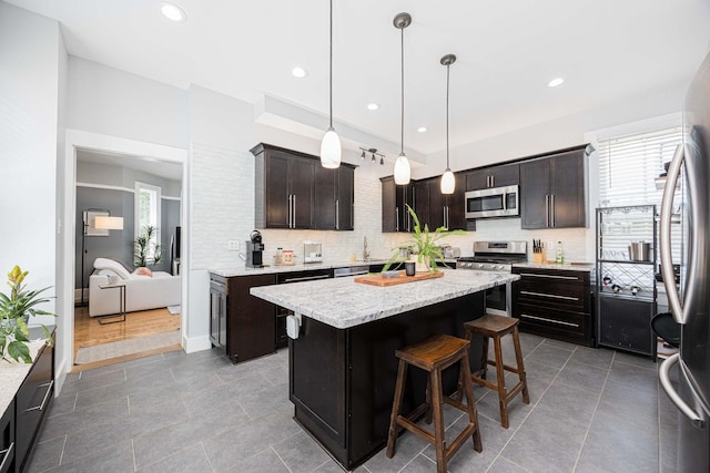 1066 City Park Ave, Columbus, OH 43206 - kitchen with appliances with stainless steel finishes, a kitchen island, backsplash, dark brown cabinets, and a kitchen breakfast bar