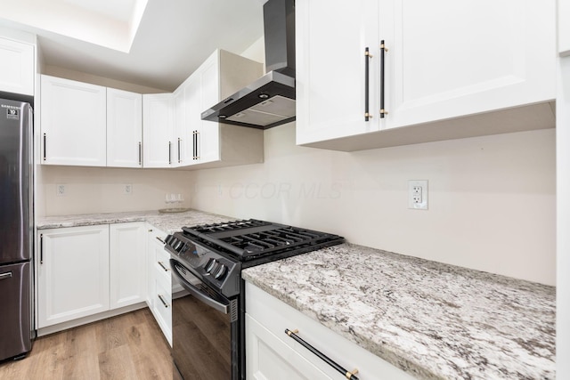 992 N Nelson Rd, Columbus, OH 43219 - kitchen featuring wall chimney range hood, black range with gas cooktop, freestanding refrigerator, light wood-type flooring, and white cabinets
