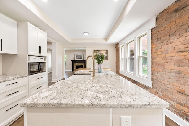 992 N Nelson Rd, Columbus, OH 43219 - kitchen featuring wood finished floors, white cabinets, light stone countertops, brick wall, and a center island with sink