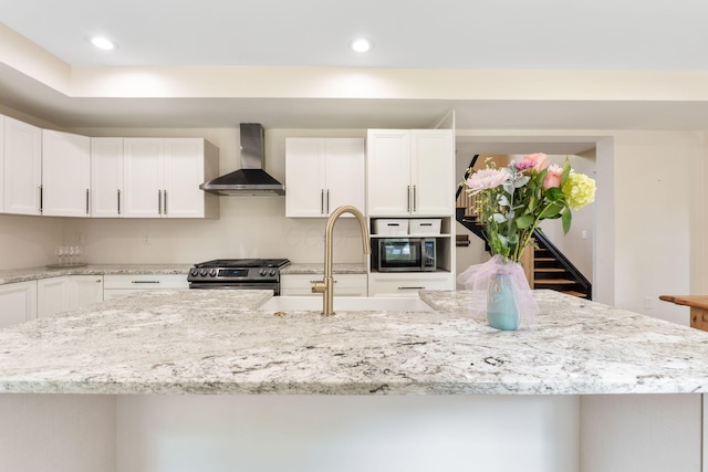 992 N Nelson Rd, Columbus, OH 43219 - kitchen featuring wall chimney range hood, appliances with stainless steel finishes, white cabinetry, light stone counters, and an island with sink