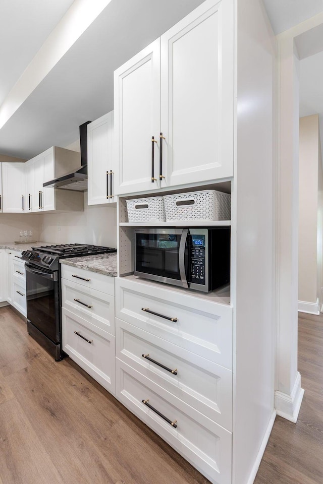 992 N Nelson Rd, Columbus, OH 43219 - kitchen with black range with gas cooktop, wall chimney range hood, wood finished floors, stainless steel microwave, and white cabinets
