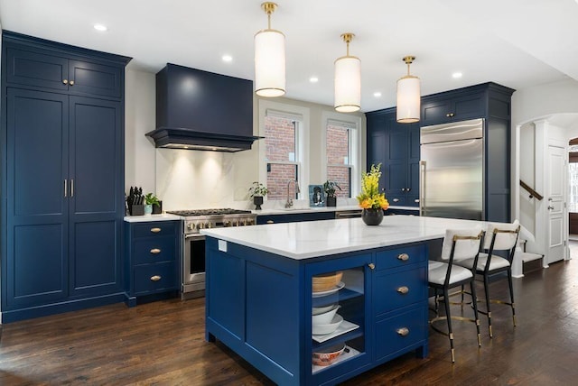 249 E Whittier St, Columbus, OH 43206 - kitchen with wall chimney range hood, high quality appliances, blue cabinetry, a kitchen bar, and recessed lighting