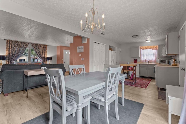 7780 Freesia St Unit 228, Blacklick, OH 43004 - dining room featuring healthy amount of natural light, light wood-style flooring, a textured ceiling, and a chandelier