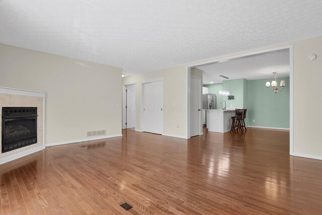 4686 Parrau Dr Unit 64A, Columbus, OH 43228 - unfurnished living room with a chandelier, a fireplace, wood finished floors, and a textured ceiling