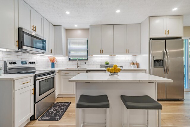 1439 Tall Meadows Dr, Columbus, OH 43223 - kitchen featuring appliances with stainless steel finishes, light wood-style floors, a kitchen breakfast bar, white cabinetry, and a textured ceiling