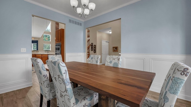 6229 Janes Way, Hilliard, OH 43026 - dining space with a chandelier, a wainscoted wall, a decorative wall, crown molding, and light wood finished floors