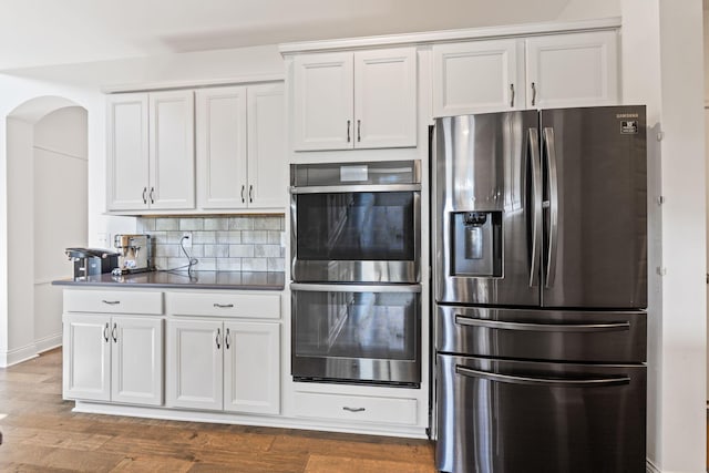 3622 Switchgrass Ct, Hilliard, OH 43026 - kitchen featuring appliances with stainless steel finishes, arched walkways, wood finished floors, white cabinets, and tasteful backsplash