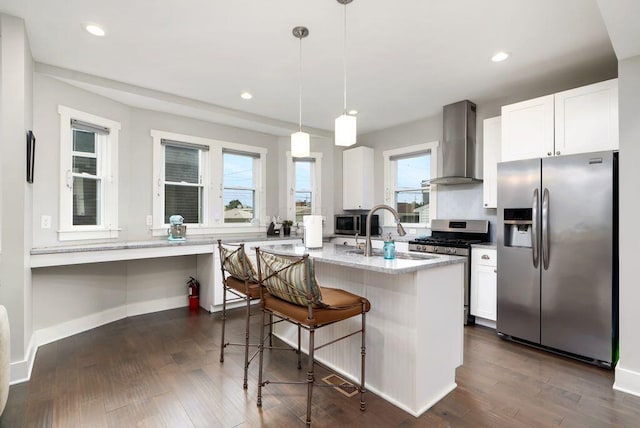 497 E Kossuth St, Columbus, OH 43206 - kitchen featuring stainless steel appliances, wall chimney range hood, white cabinets, a center island with sink, and a kitchen bar