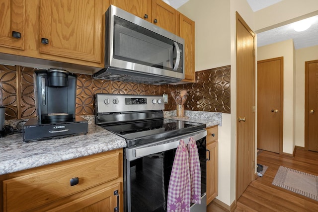 50 Bazler Ln, South Bloomfield, OH 43103 - kitchen featuring stainless steel appliances, light wood finished floors, decorative backsplash, brown cabinetry, and light stone counters