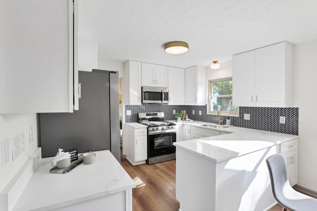 8139 Storrow Dr, Westerville, OH 43081 - kitchen featuring appliances with stainless steel finishes, a peninsula, backsplash, white cabinets, and a textured ceiling