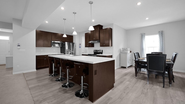336 Onyx Ln, Delaware, OH 43015 - kitchen with appliances with stainless steel finishes, dark brown cabinets, light countertops, a kitchen island with sink, and light wood-type flooring