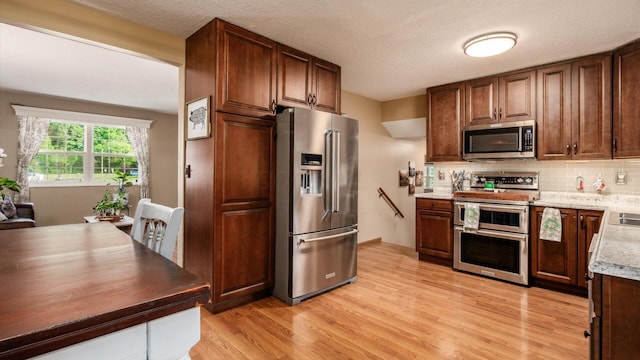637 Livingston Ct, Heath, OH 43056 - kitchen with stainless steel appliances, light wood-type flooring, backsplash, light stone counters, and a textured ceiling
