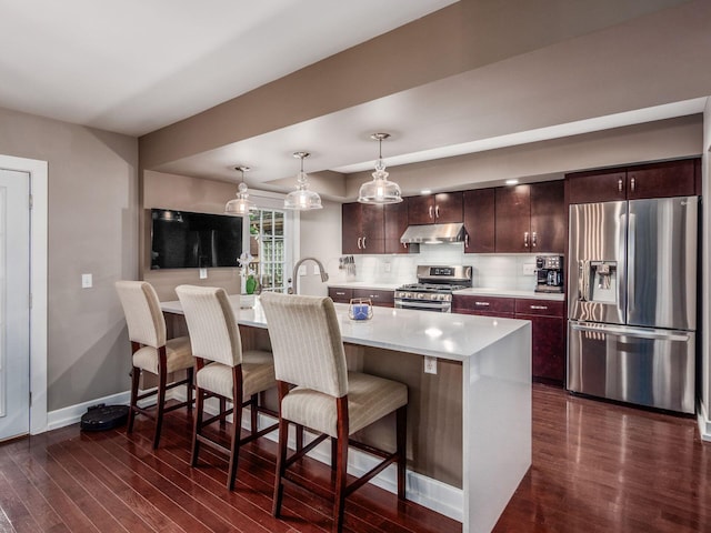 1243 Harrison Ave, Columbus, OH 43201 - kitchen featuring appliances with stainless steel finishes, under cabinet range hood, light countertops, dark wood finished floors, and a breakfast bar area