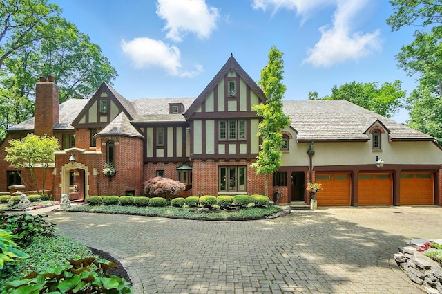 2475 Signal Hill Rd, Springfield, OH 45504 - tudor home featuring stucco siding, a chimney, decorative driveway, brick siding, and an attached garage