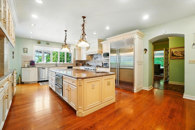 2475 Signal Hill Rd, Springfield, OH 45504 - kitchen with built in appliances, arched walkways, decorative backsplash, an island with sink, and custom range hood
