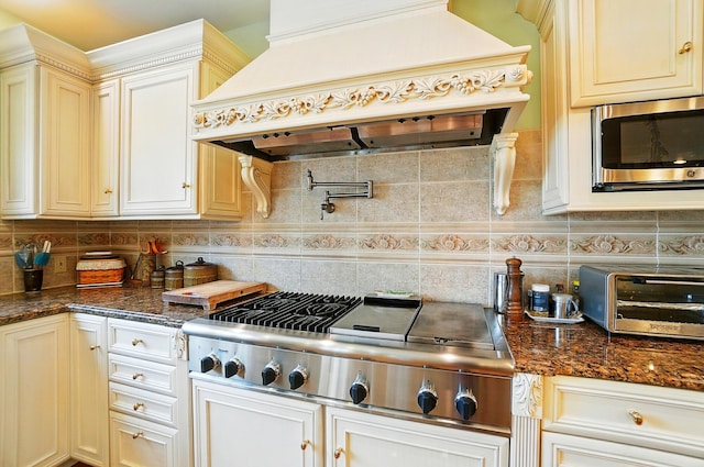 2475 Signal Hill Rd, Springfield, OH 45504 - kitchen with custom range hood, stainless steel appliances, tasteful backsplash, dark stone counters, and cream cabinetry