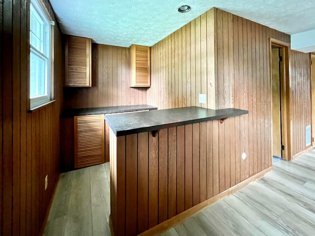 5200 Williamsburg Cir, Hilliard, OH 43026 - kitchen featuring dark countertops, a textured ceiling, light wood-style flooring, wooden walls, and brown cabinets