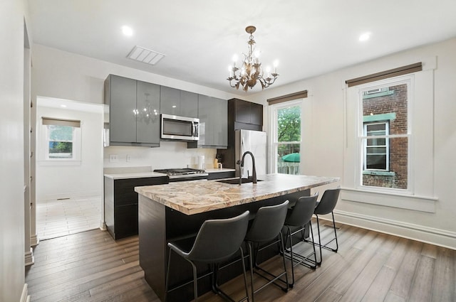 626 S 22nd St, Columbus, OH 43205 - kitchen with stainless steel microwave, an island with sink, a chandelier, light countertops, and dark wood-style floors