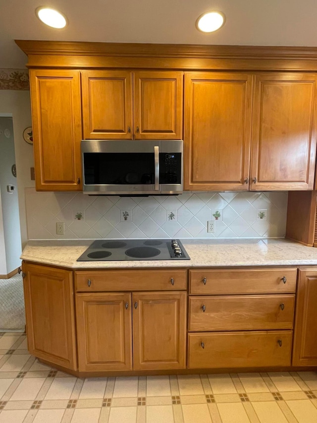 2666 Eugene Ave, Grove City, OH 43123 - kitchen with stainless steel microwave, black electric stovetop, brown cabinetry, light flooring, and backsplash