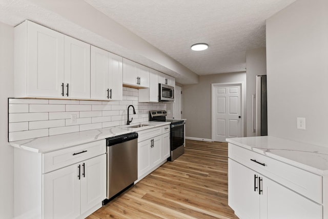 1664 S Champion Ave, Columbus, OH 43207 - kitchen with appliances with stainless steel finishes, backsplash, light wood-style flooring, white cabinets, and light stone countertops