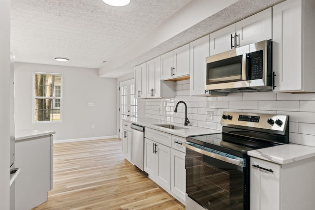 1664 S Champion Ave, Columbus, OH 43207 - kitchen featuring appliances with stainless steel finishes, a textured ceiling, backsplash, white cabinetry, and light wood-style floors