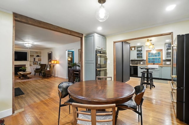 2620 Edgevale Rd, Columbus, OH 43221 - dining space with light wood-style floors, a brick fireplace, built in shelves, beam ceiling, and crown molding