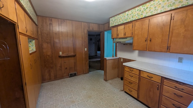 708 Fairview Ave, Galion, OH 44833 - kitchen featuring brown cabinets, under cabinet range hood, light countertops, tasteful backsplash, and wood walls
