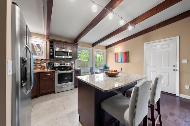 2474 Bristol Rd, Columbus, OH 43221 - kitchen with appliances with stainless steel finishes, decorative backsplash, a kitchen breakfast bar, beamed ceiling, and light stone countertops