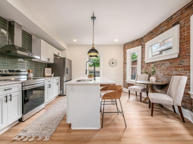 935 S Ohio Ave, Columbus, OH 43206 - kitchen featuring appliances with stainless steel finishes, wall chimney exhaust hood, white cabinets, light wood-type flooring, and light countertops