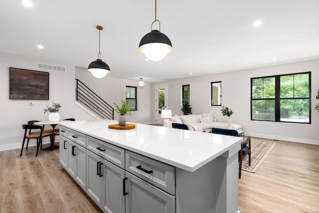 546 W Town St, Columbus, OH 43215 - kitchen featuring gray cabinets, light countertops, a kitchen island, light wood finished floors, and decorative light fixtures