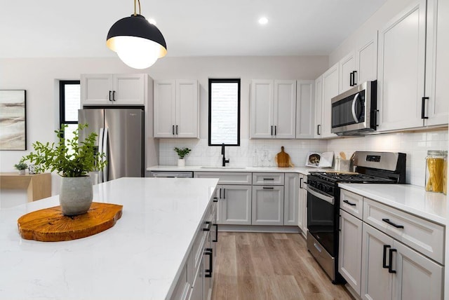 546 W Town St, Columbus, OH 43215 - kitchen featuring appliances with stainless steel finishes, decorative backsplash, light stone counters, light wood-style floors, and decorative light fixtures