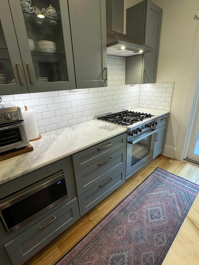 489 W 4th Ave, Columbus, OH 43201 - kitchen featuring appliances with stainless steel finishes, wall chimney exhaust hood, gray cabinets, light wood-style flooring, and tasteful backsplash