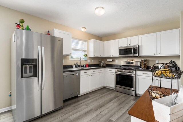 208 Dowler Dr, South Bloomfield, OH 43103 - kitchen featuring appliances with stainless steel finishes, dark countertops, light wood-style flooring, and white cabinets