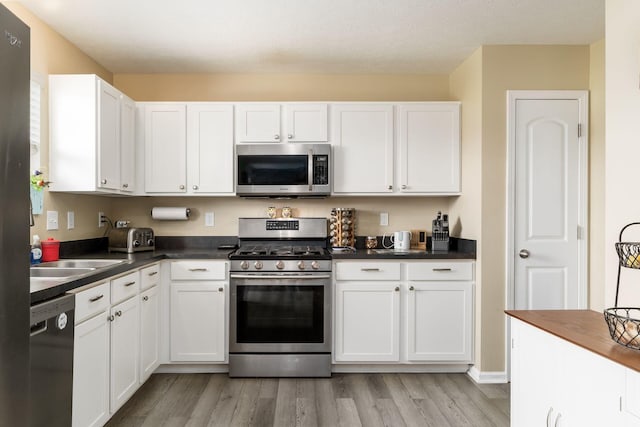 208 Dowler Dr, South Bloomfield, OH 43103 - kitchen featuring stainless steel appliances, light wood-type flooring, white cabinets, and dark countertops