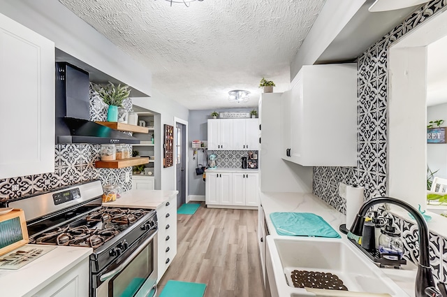 599 S Brinker Ave, Columbus, OH 43204 - kitchen featuring stainless steel range with gas cooktop, wall chimney range hood, light wood-style flooring, white cabinets, and backsplash
