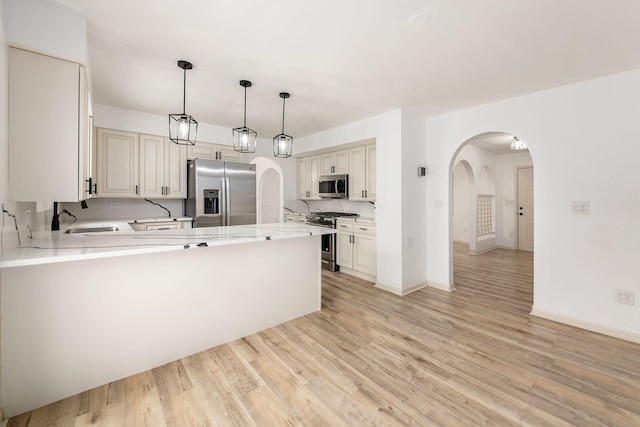 1571 Vinton Ave, Columbus, OH 43220 - kitchen featuring stainless steel appliances, arched walkways, a peninsula, light wood finished floors, and hanging light fixtures