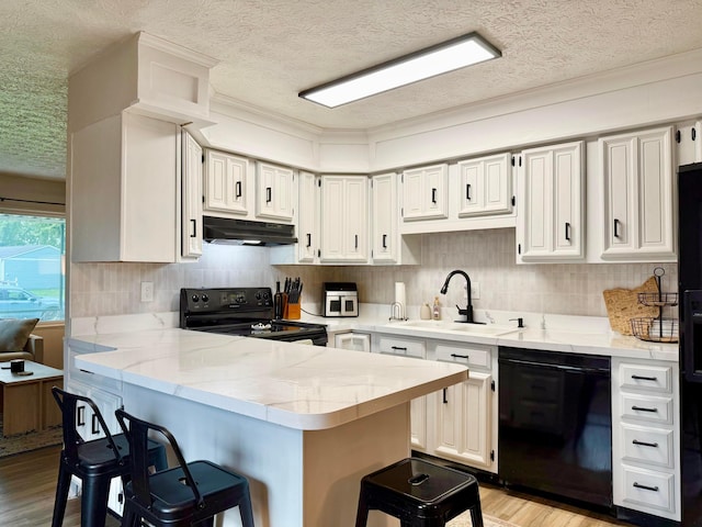 3811 Bradford Dr, Hilliard, OH 43026 - kitchen with black appliances, under cabinet range hood, a textured ceiling, a peninsula, and a kitchen breakfast bar