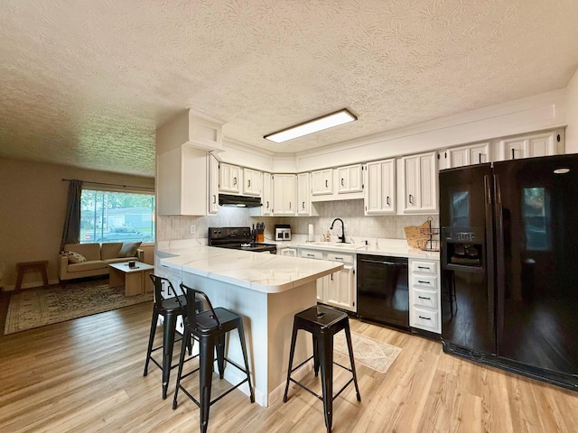 3811 Bradford Dr, Hilliard, OH 43026 - kitchen featuring black appliances, under cabinet range hood, light wood finished floors, a peninsula, and a textured ceiling