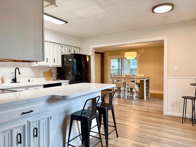 3811 Bradford Dr, Hilliard, OH 43026 - kitchen with black fridge with ice dispenser, light wood-type flooring, a kitchen breakfast bar, a textured ceiling, and a wainscoted wall