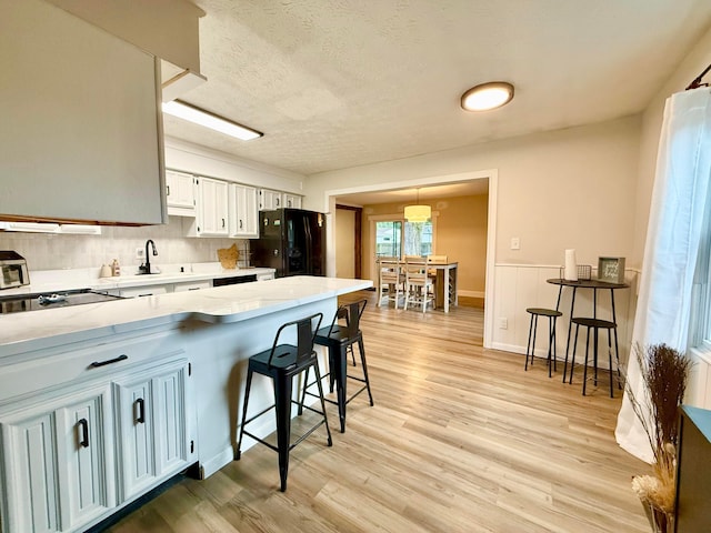 3811 Bradford Dr, Hilliard, OH 43026 - kitchen featuring black appliances, light countertops, light wood-style flooring, a breakfast bar area, and wainscoting