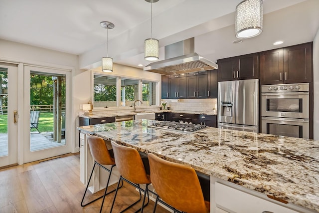 1318 Hickory Ridge Ln, Columbus, OH 43235 - kitchen featuring appliances with stainless steel finishes, wall chimney exhaust hood, light stone counters, light wood-type flooring, and a kitchen bar