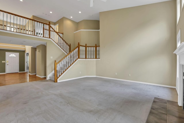 7511 Windsor Dr, Dublin, OH 43016 - unfurnished living room with carpet flooring, a towering ceiling, stairs, a fireplace with flush hearth, and a ceiling fan