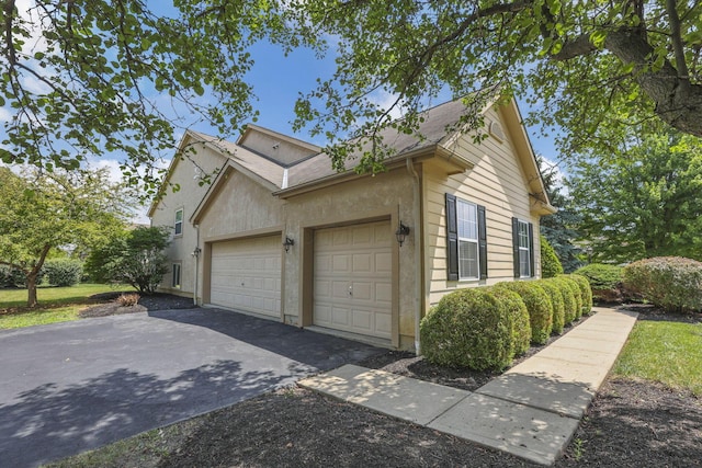 7511 Windsor Dr, Dublin, OH 43016 - view of side of property featuring an attached garage, stucco siding, and asphalt driveway