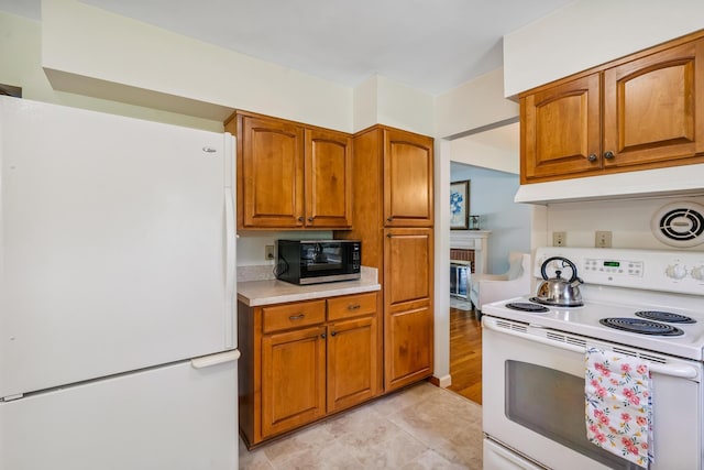 6750 Schreiner St E, Worthington, OH 43085 - kitchen with white appliances, brown cabinetry, light countertops, under cabinet range hood, and a brick fireplace