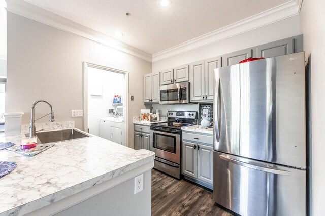6028 Inishmore Ln, Dublin, OH 43017 - kitchen with appliances with stainless steel finishes, washer and clothes dryer, gray cabinets, ornamental molding, and dark wood-style floors