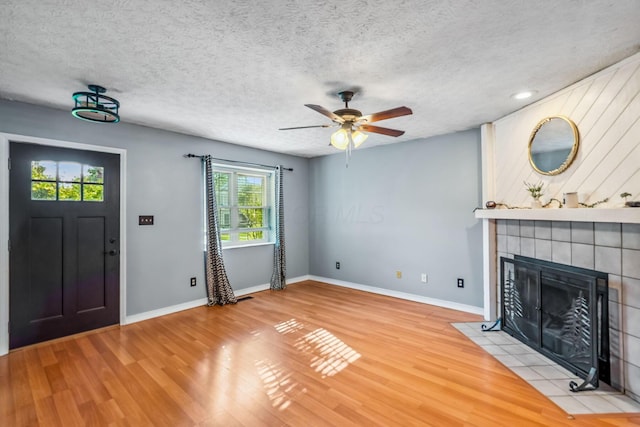 4905 Mckenna Ct, Columbus, OH 43221 - unfurnished living room with light wood-style floors, ceiling fan, a tiled fireplace, and a textured ceiling