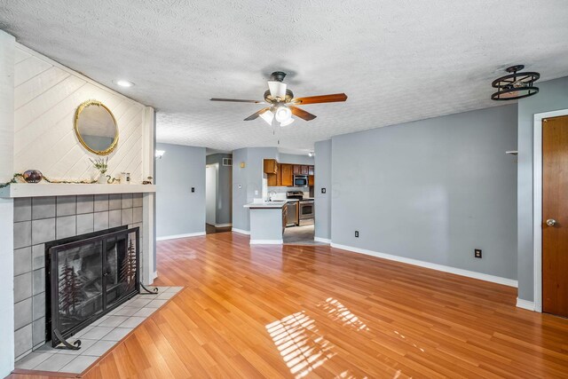 4905 Mckenna Ct, Columbus, OH 43221 - unfurnished living room featuring a tiled fireplace, a ceiling fan, light wood-style flooring, and a textured ceiling